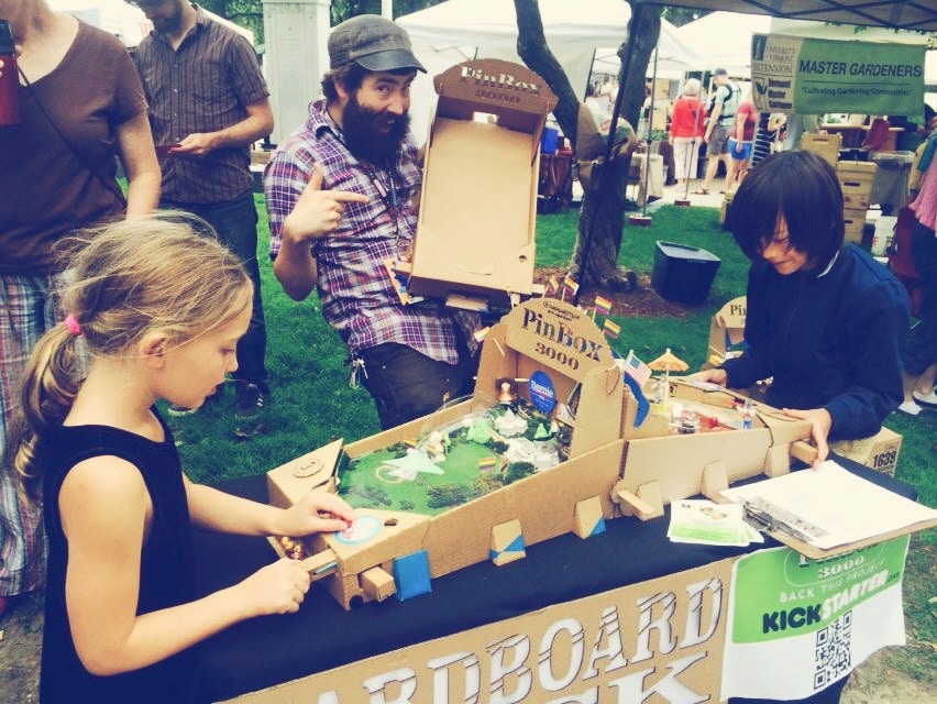 boy and a girl playing a cardboard pin ball game