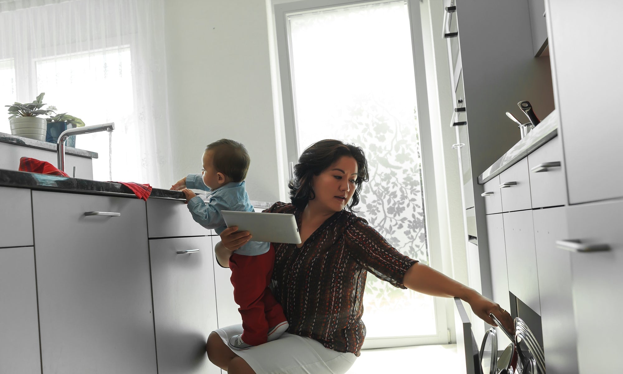 A Mother working in kitchen holding her baby