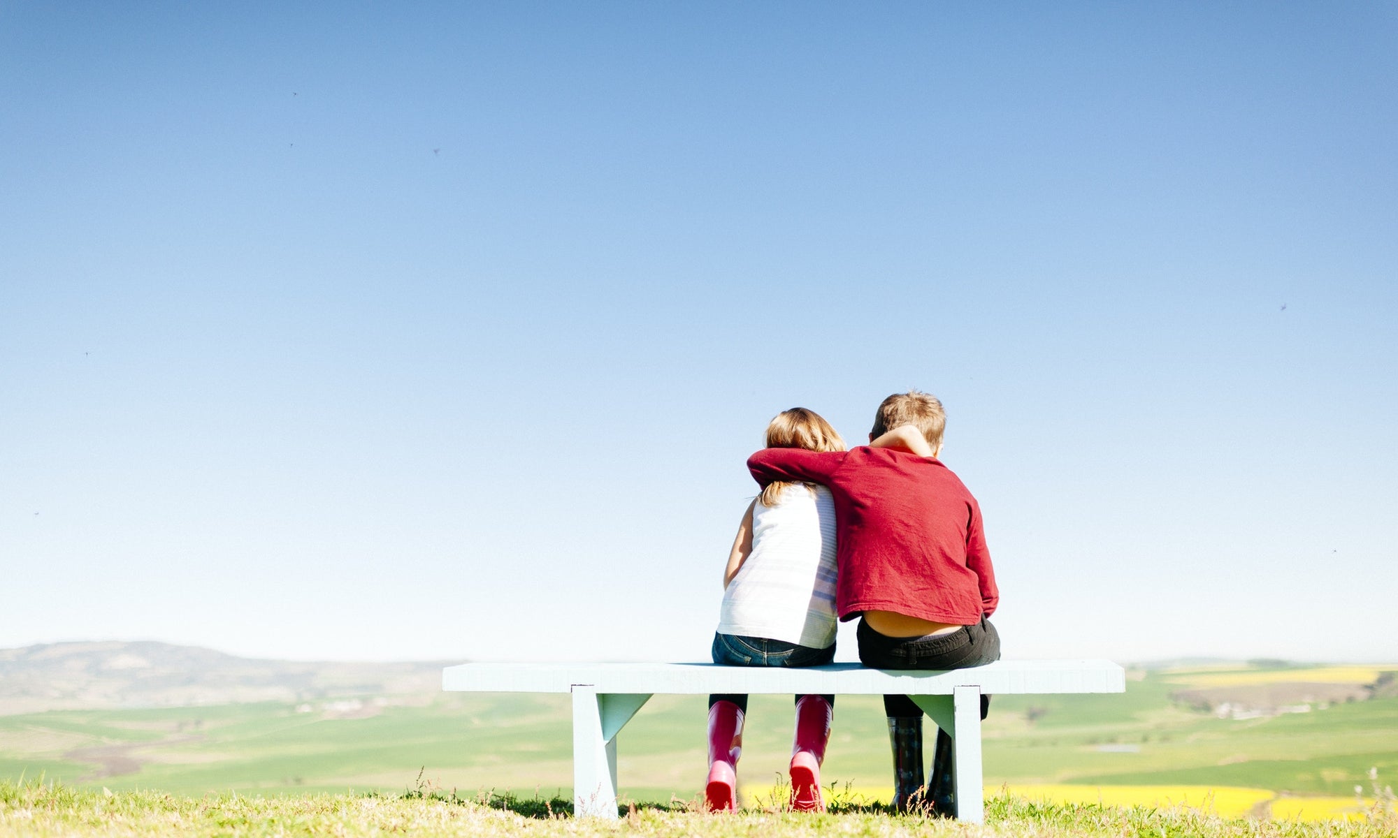 rear view of boy and girl sitting on bench at  field