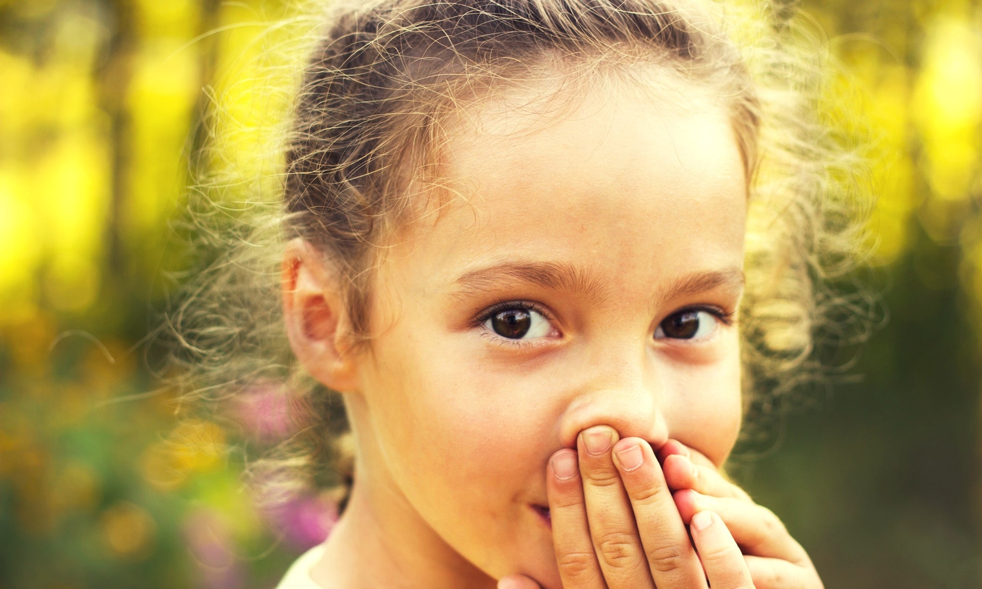 little girl covering her mouth with her hands