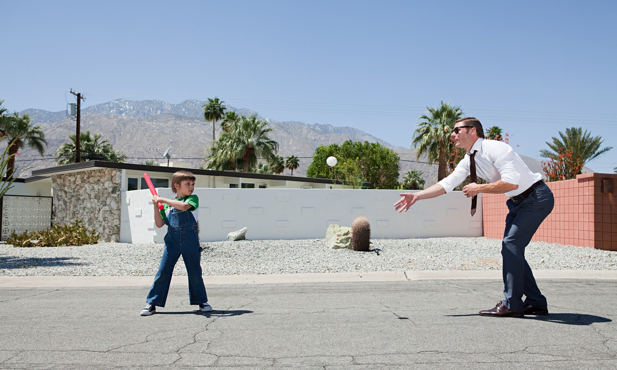 a boy playing with a man in a road infront of a house with white and red walls