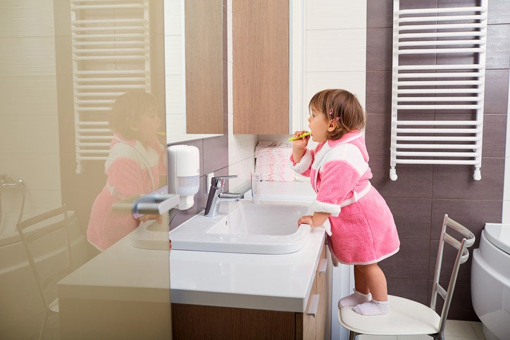 little baby is standing on a chair in the bathroom wrapped in an pink towel with a toothbrush and brushes her teeth