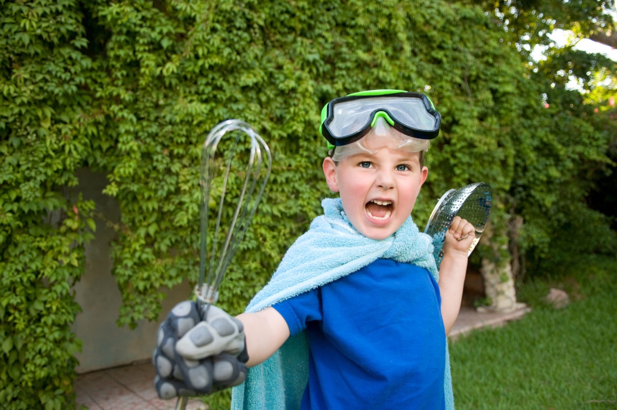 young boy wearning bath towel in shoulders with kitchen equipments in hands