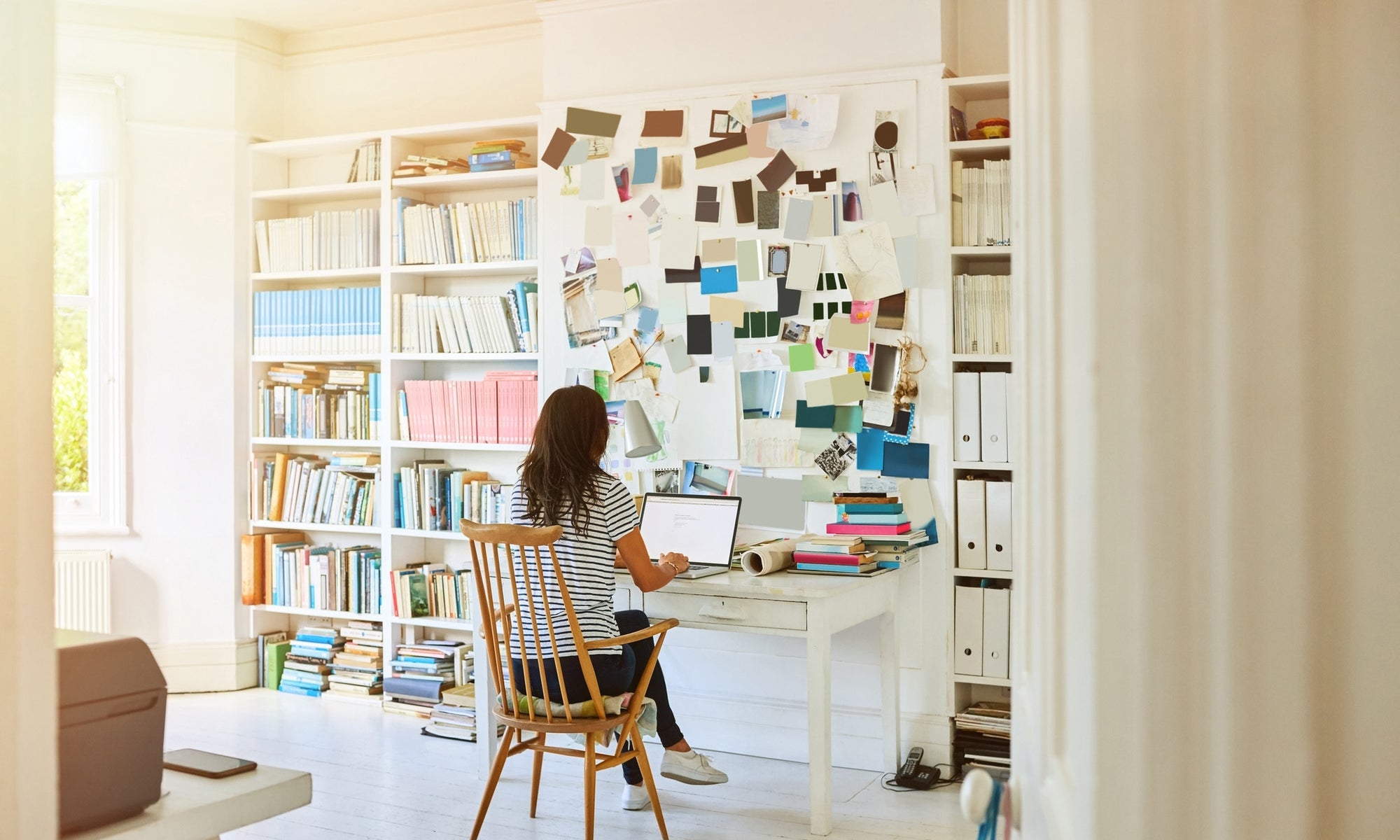 rear view of young lady working on laptop in study room with books