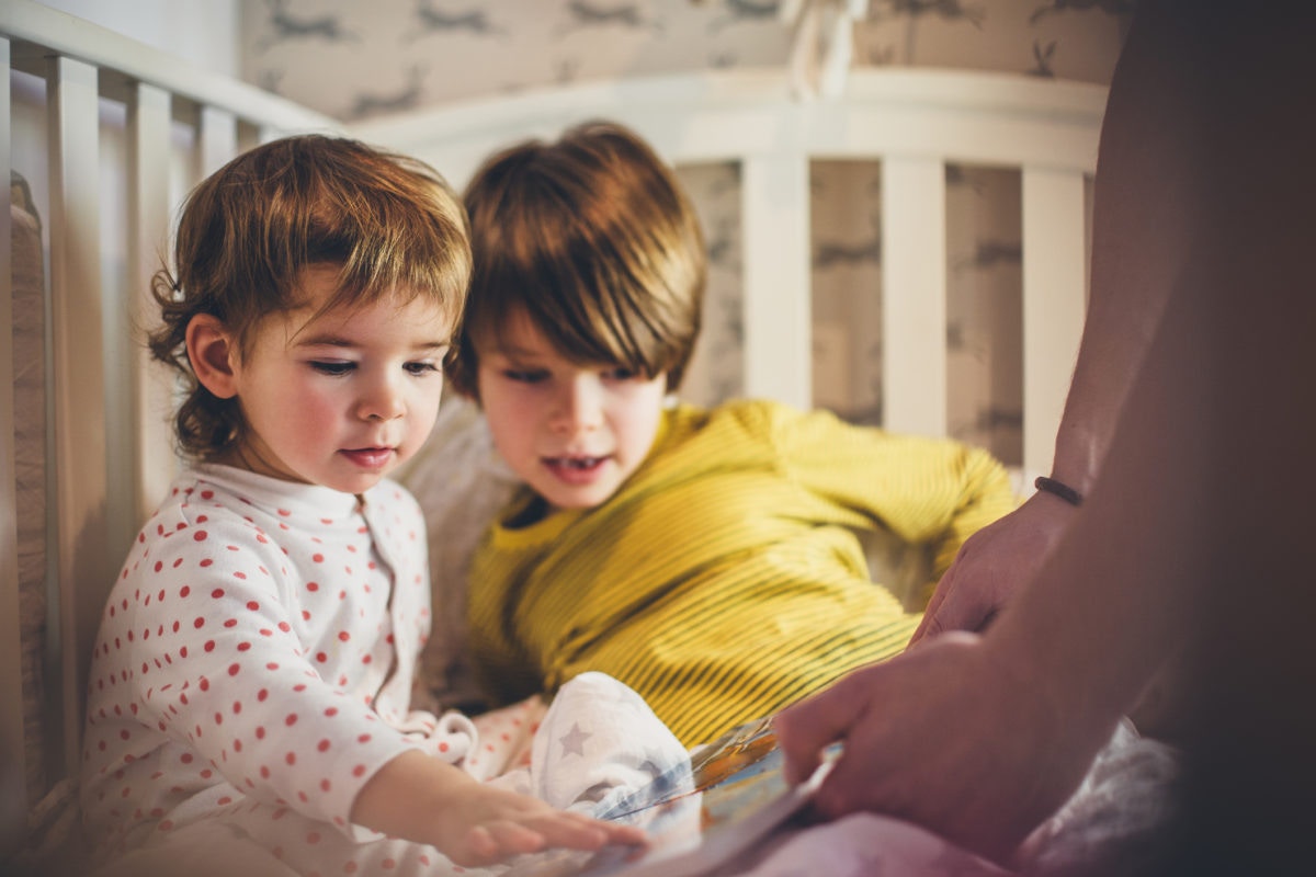 Brother and sister read a book sitting in bed