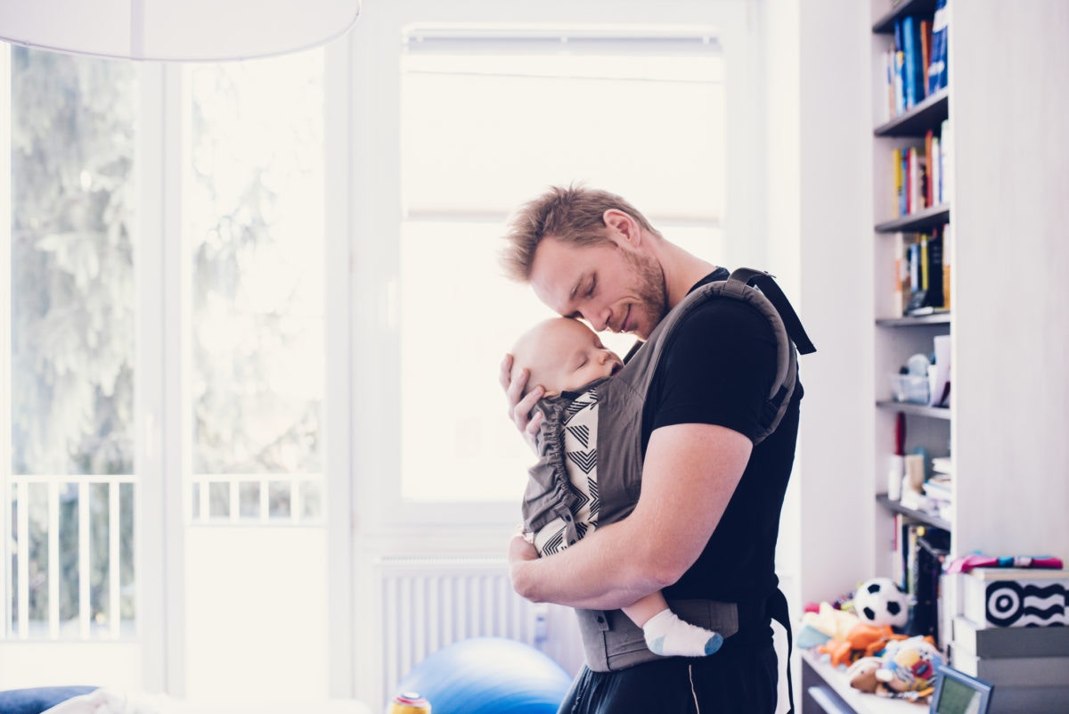 Smiling father hugging his baby in a carrier