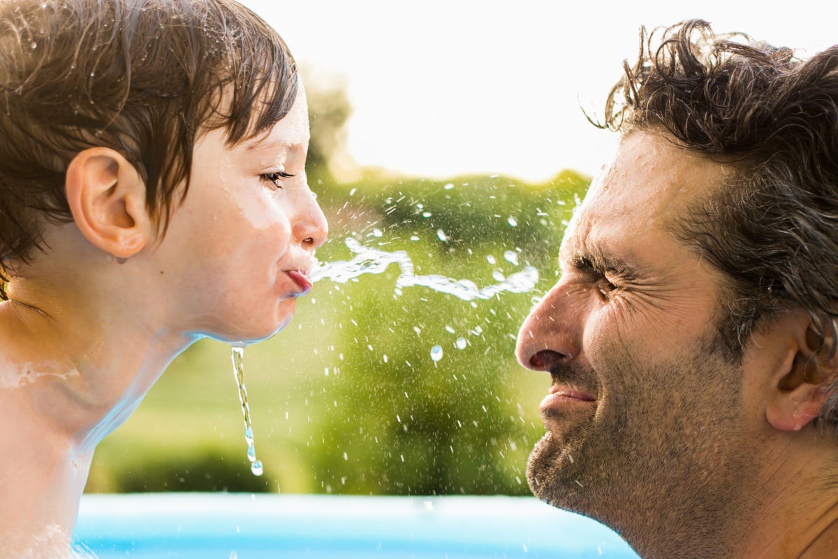 A kid is spitting water from mouth on his father's face