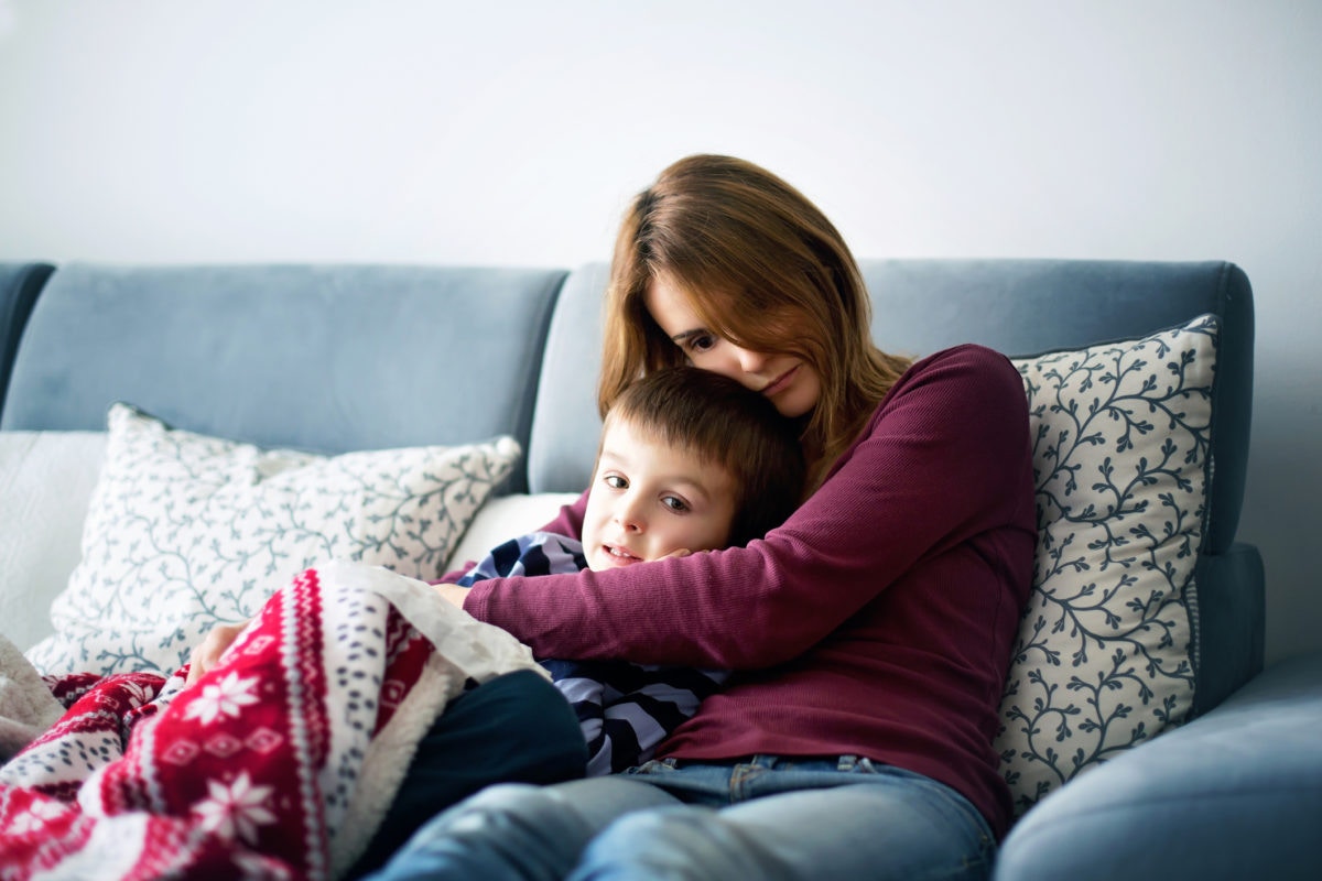 Sad mother hugging her child on the sofa in a blanket