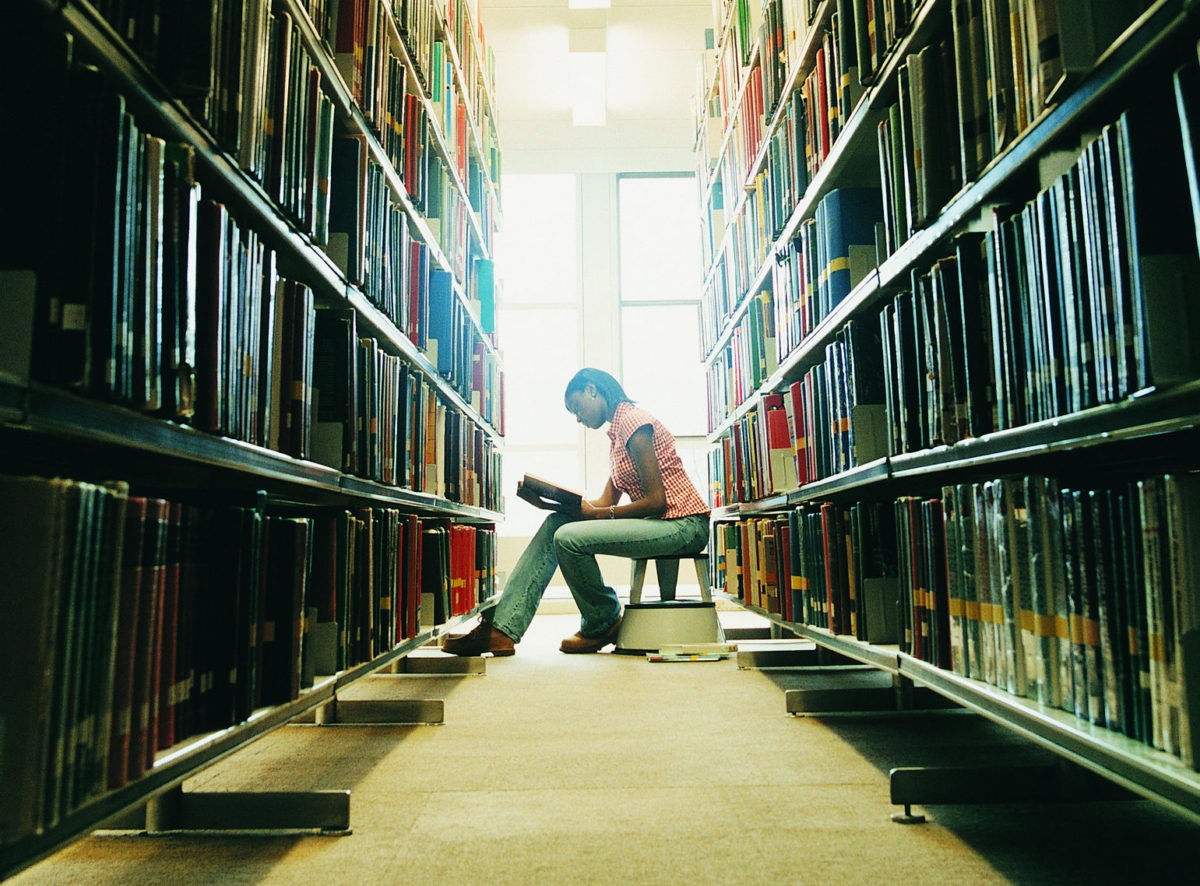 young lady sitting on library and looking for books at bookshelf full of books