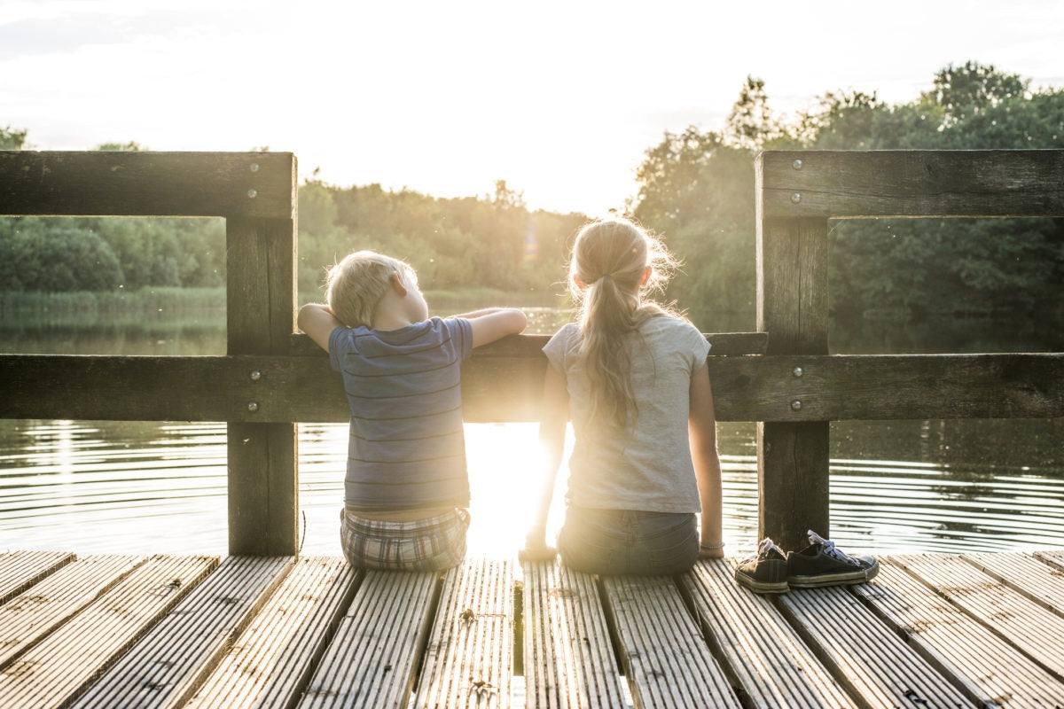 brother and sister sitting on pier over lake