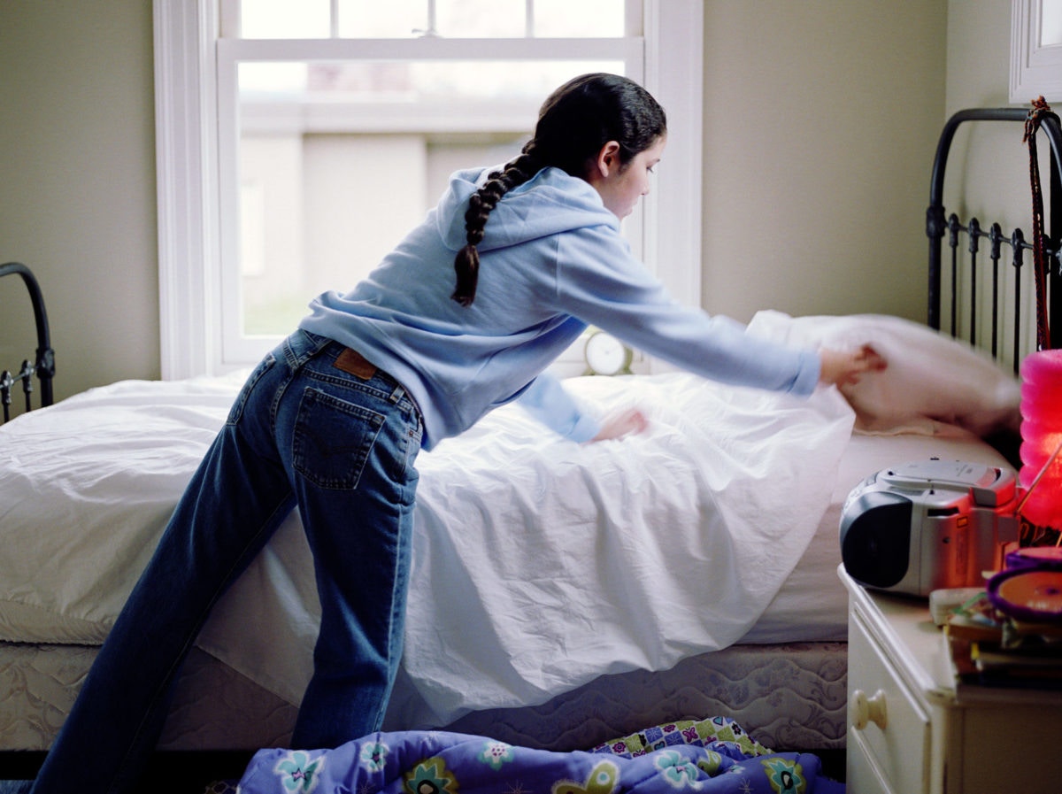 woman putting blanket on bed at home 