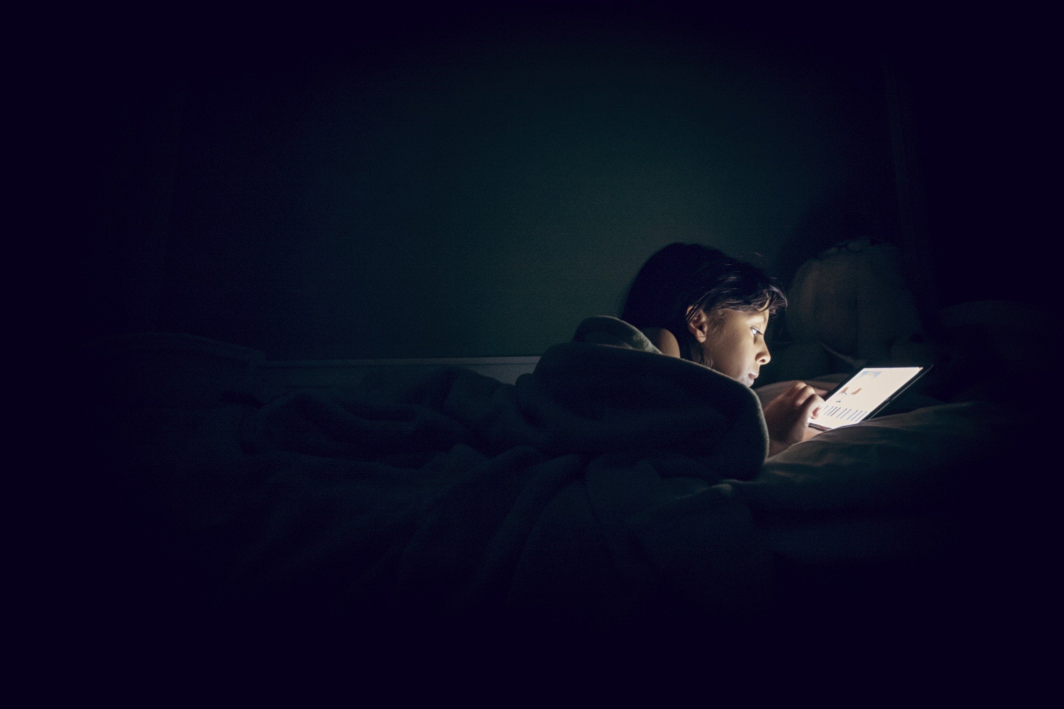 A person using tab on the bed at dark