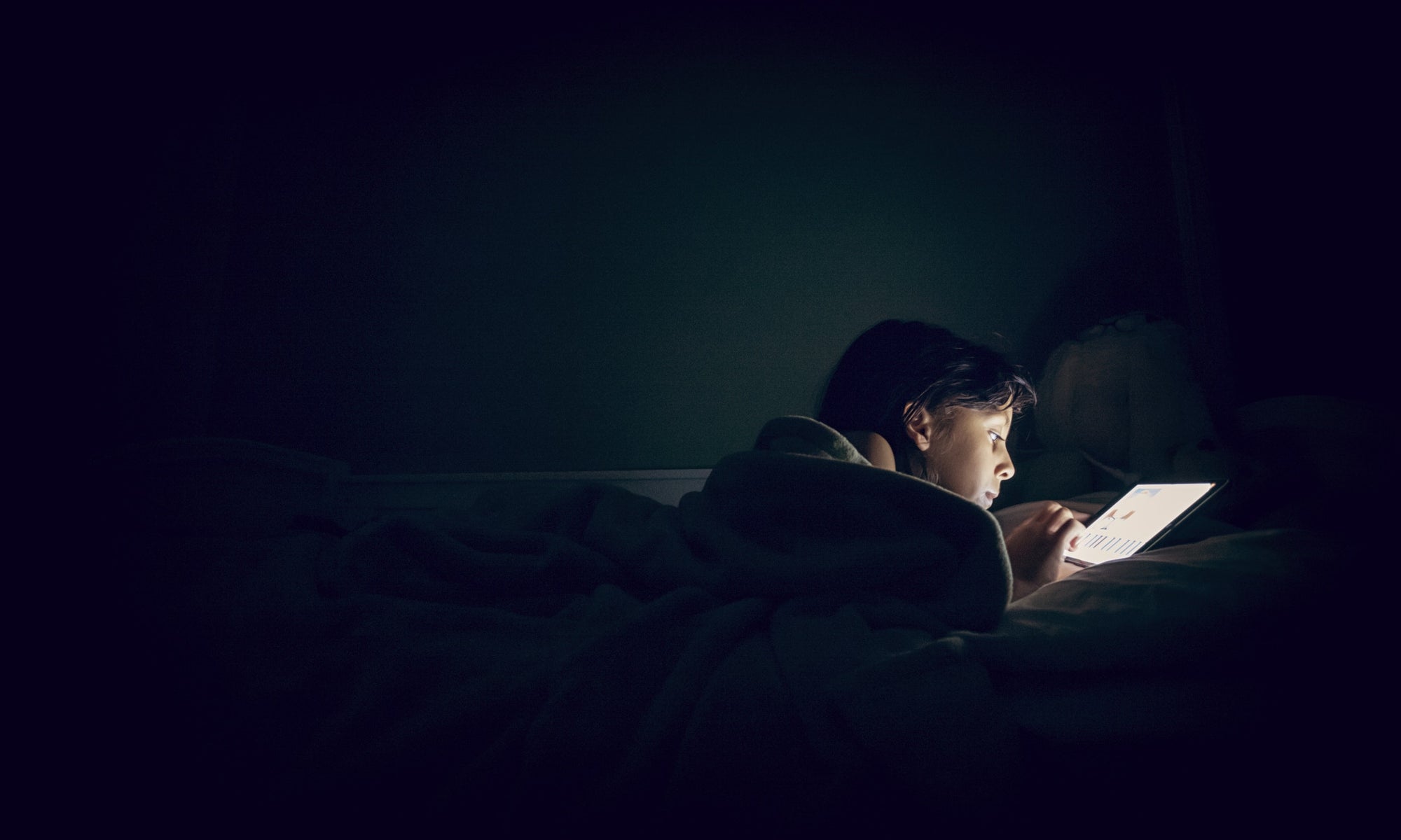 A person using tab on the bed at dark