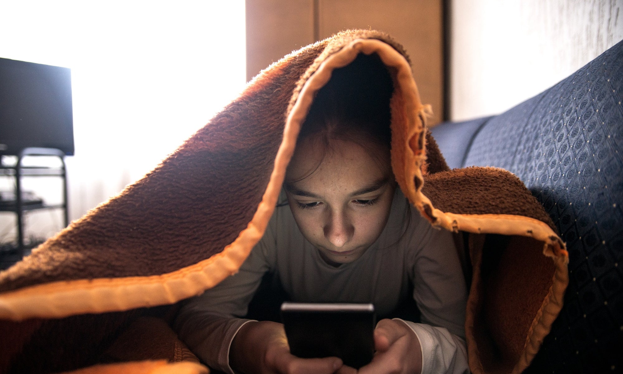 A girl using phone under the blanket