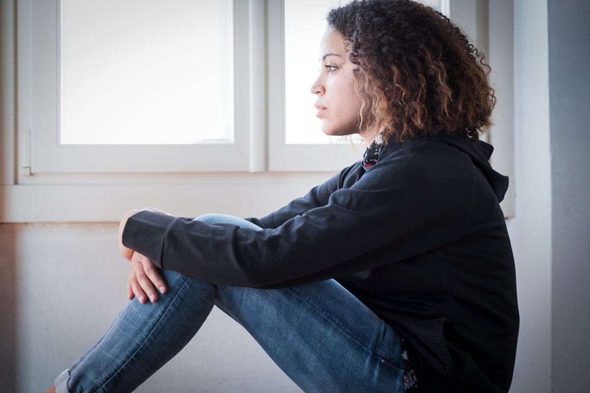 young girl sitting on floor hugging knees looking at distance