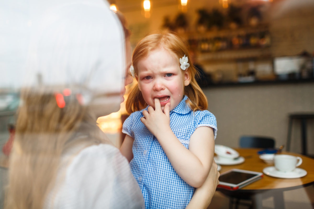 mom holding her child who is crying in a coffee shop