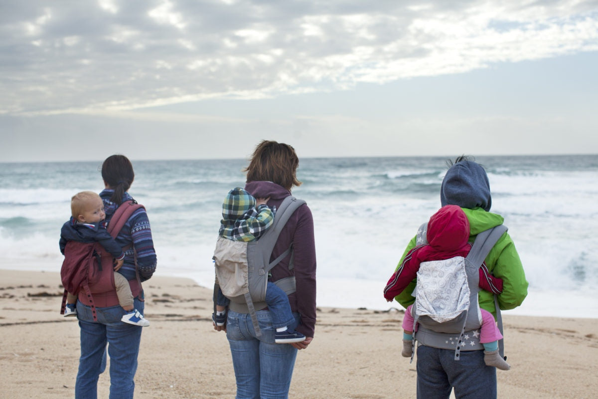 Group of mother carrying their babies backside and standing infront of ocean