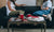 Two girls sitting in a sofa with cups ,tab and books placed on a table