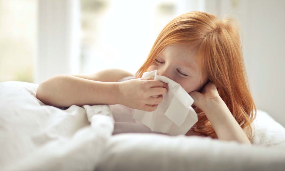 kid blowing her nose in bed