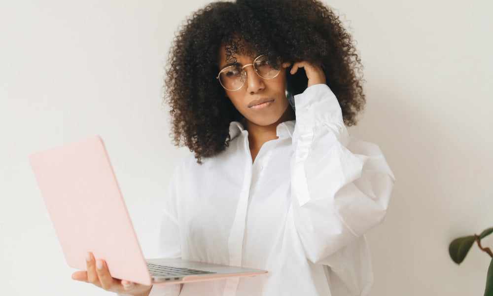 woman looking at computer holding phone