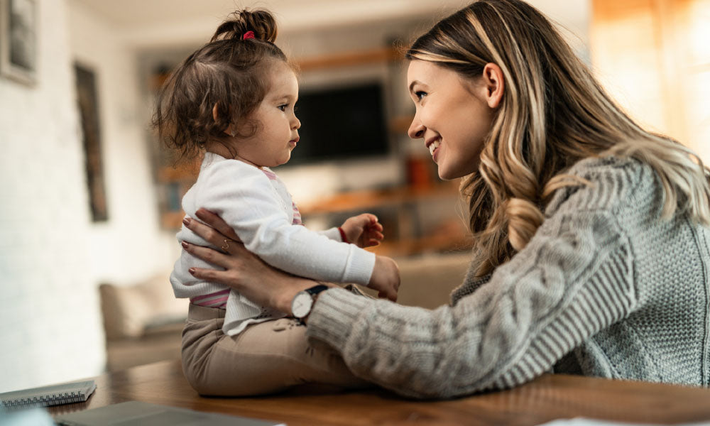 young happy mother talking to her small daughter at home